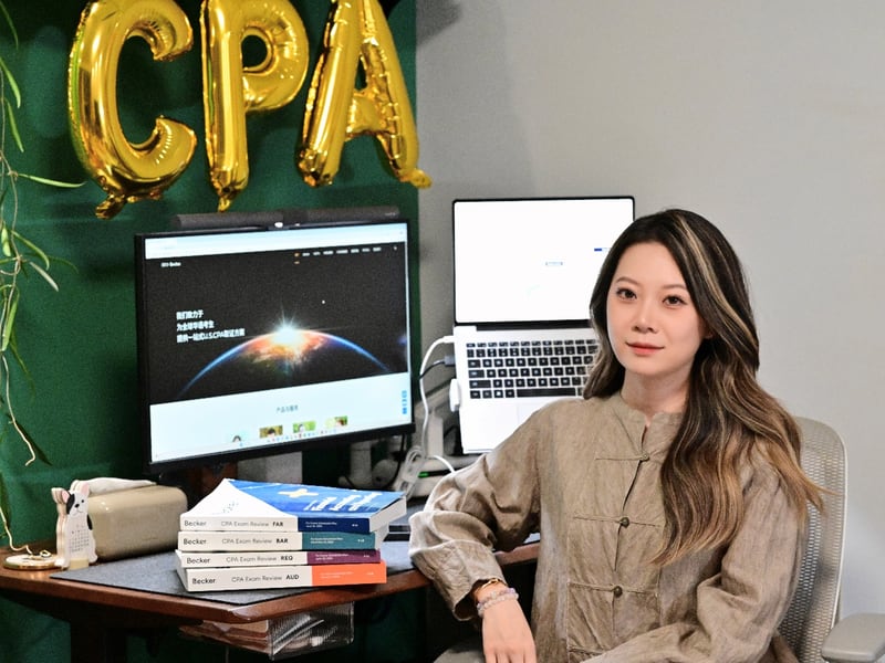 樊同学家居书桌合影：手书背景金色 CPA 气球字 + Becker 教材塔 + 双屏备考工作站
