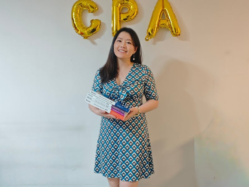 Amber 同学合影：手持 Becker USCPA 教材塔，背景金色 CPA 气球字